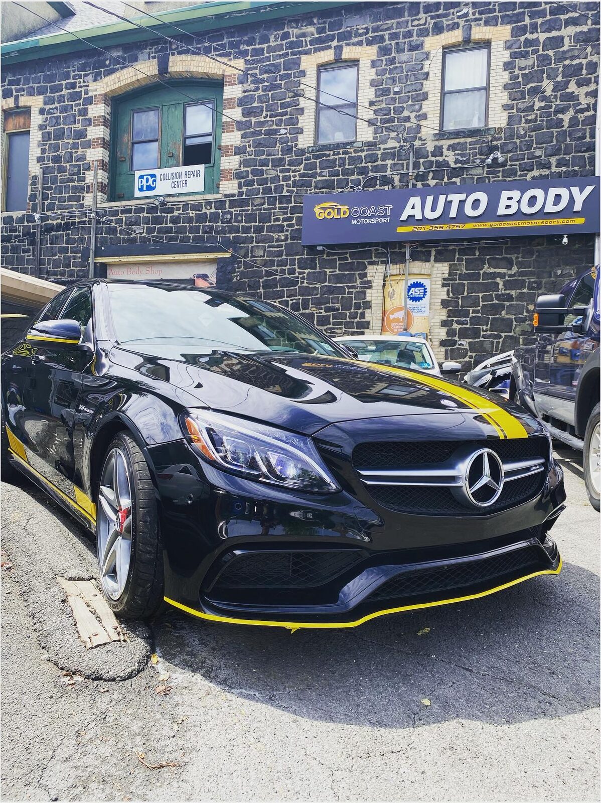 Black Mercedes-AMG C63 with a yellow accent stripe along the front splitter, parked in front of the Gold Coast Motorsport shop.