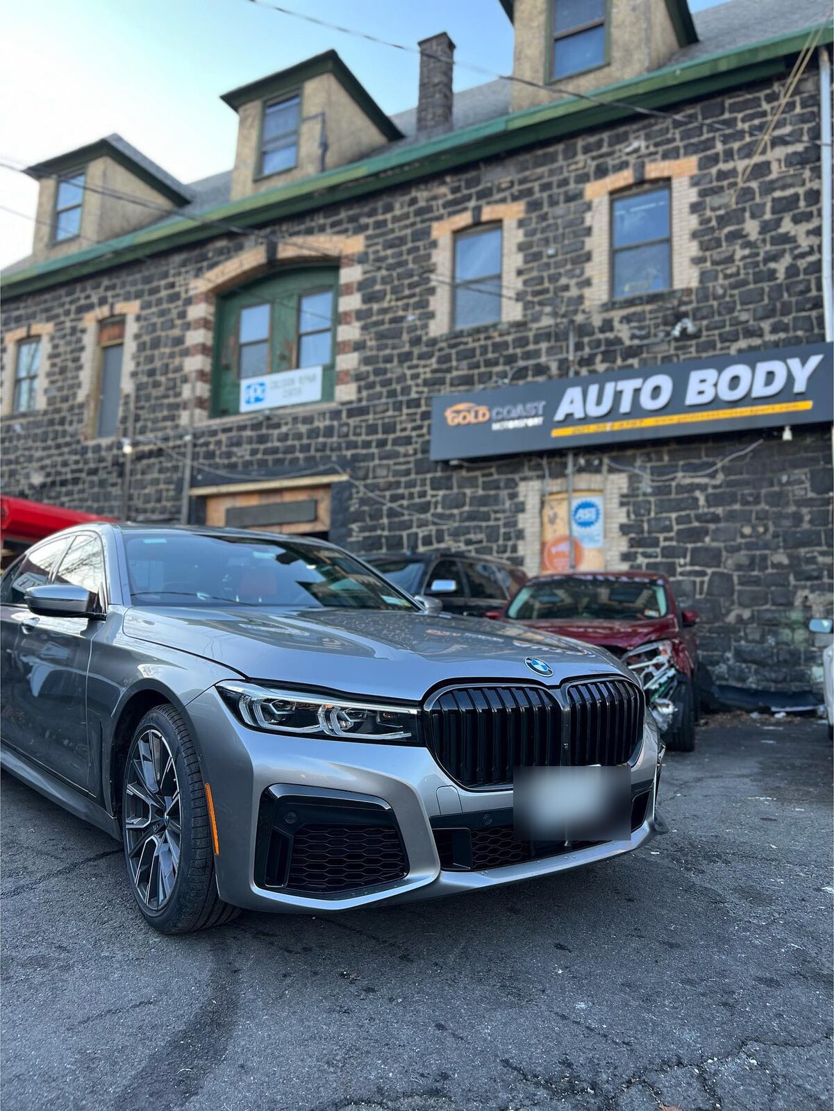 Grey BMW 7 Series parked in front of the Gold Coast Motorsport shop, front license plate blurred.