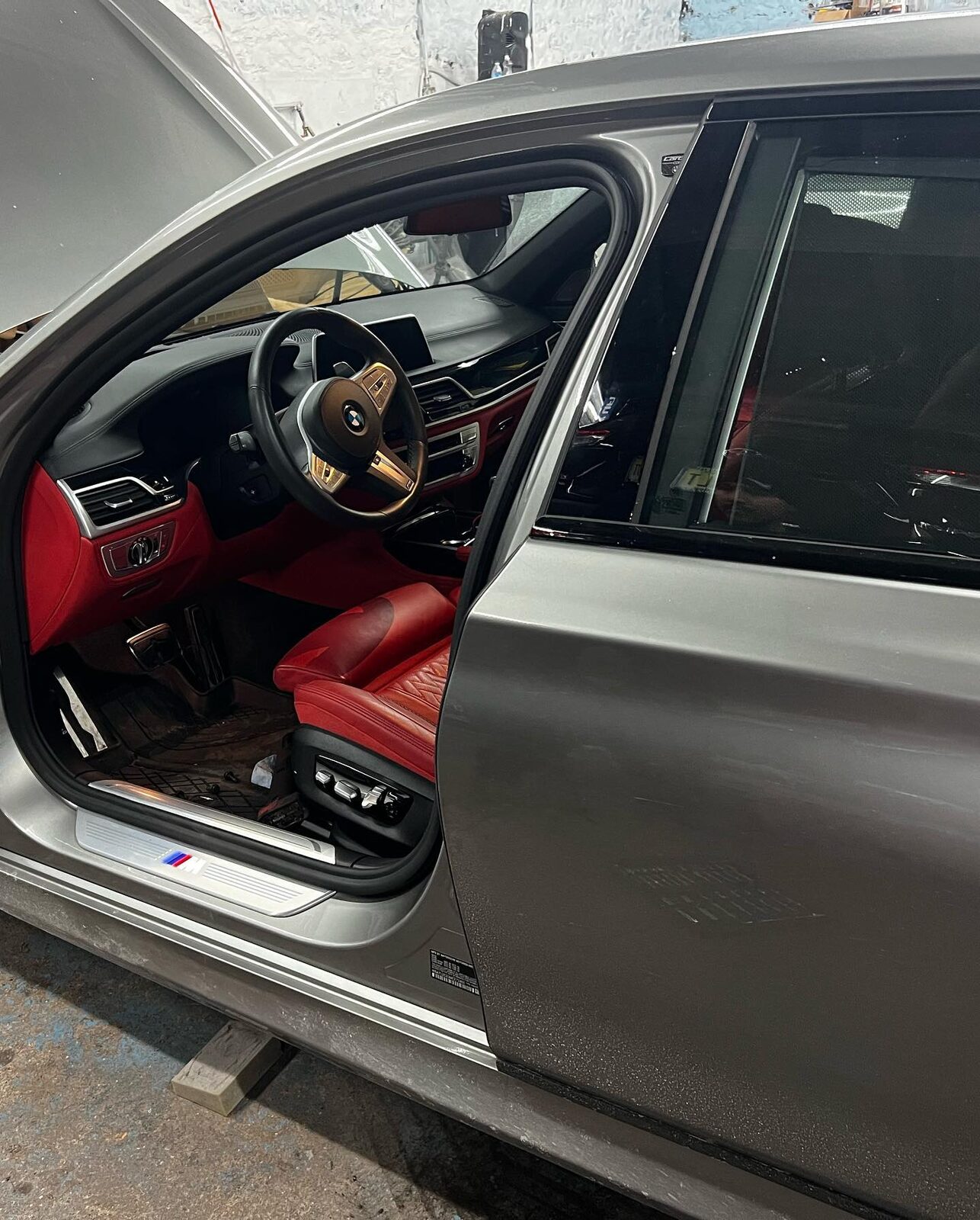 Open driver door of the grey BMW 7 Series showing the red leather interior after reassembly.